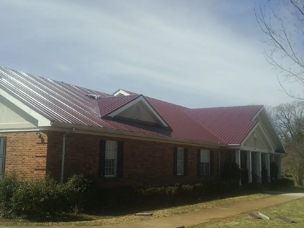 Red metal roof with gabled entries on a long brick building, from a Hail Damage Roof Repair job in Mc Donough