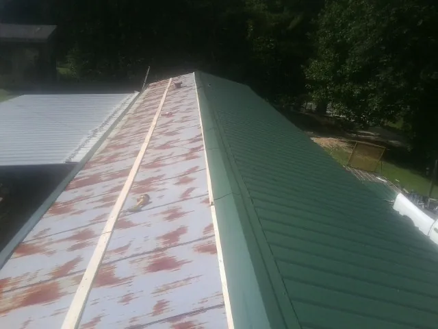 Old rusted panels beside newly installed green metal roofing — Wind Damage Roof Repair by Roofing Brothers in Mc Donough