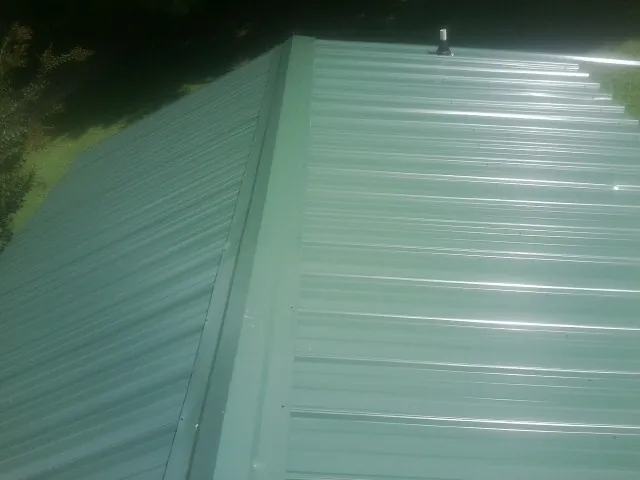 New green metal panels meeting at the ridge of a roof — Flat Roof Repair work by our crew in Mc Donough
