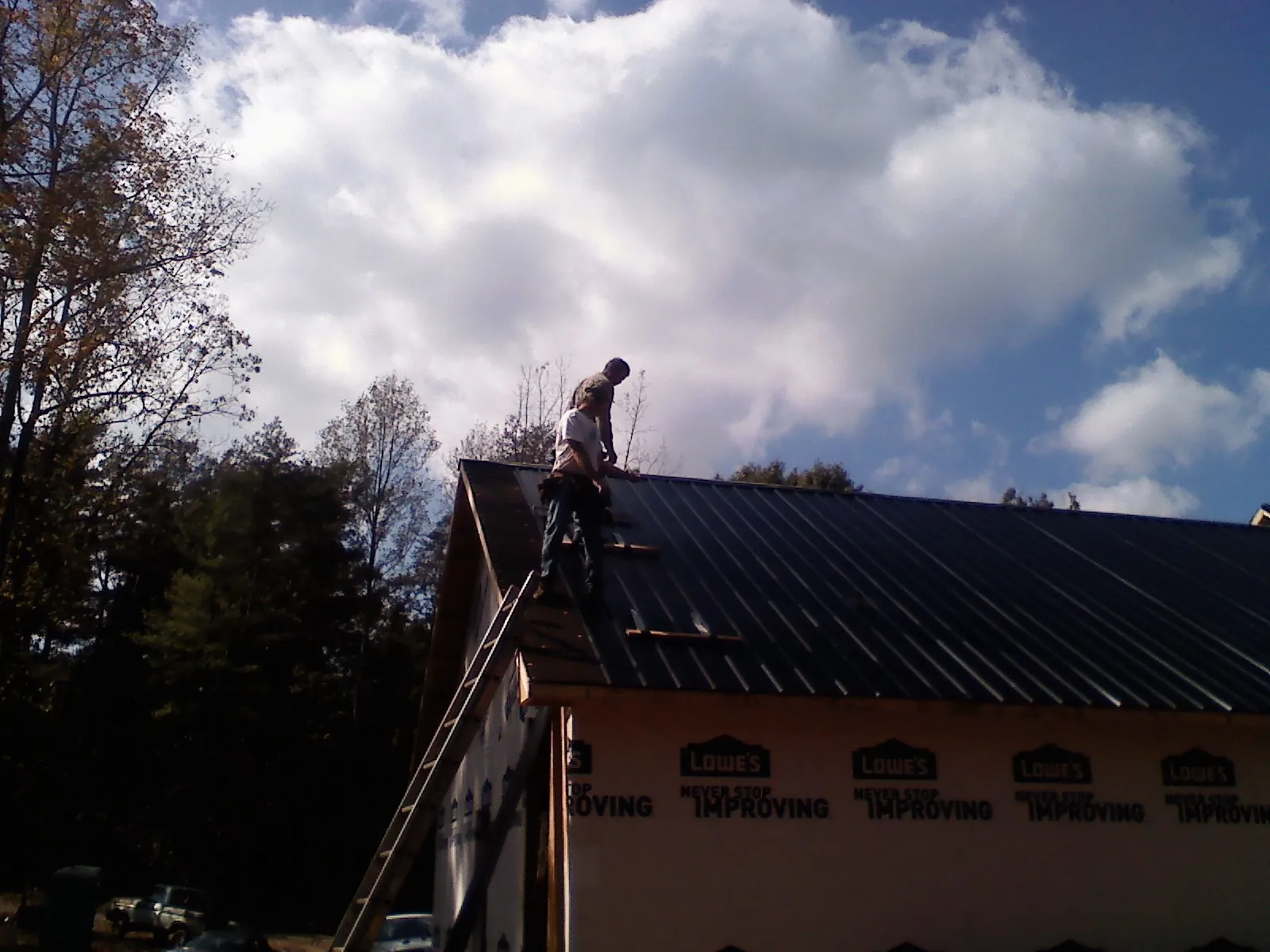 Roofer fastening dark metal panels high against a cloudy sky, from a Roof Inspection job in Mc Donough