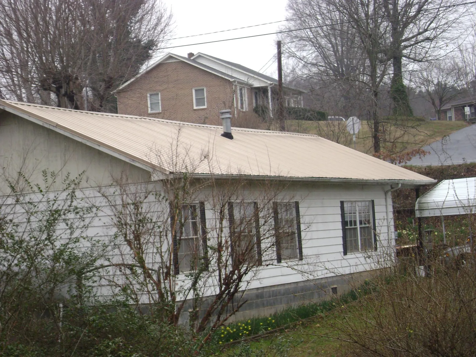 Tan metal roof on a white sided house set into a hillside — Commercial Roofing by Roofing Brothers in Mc Donough