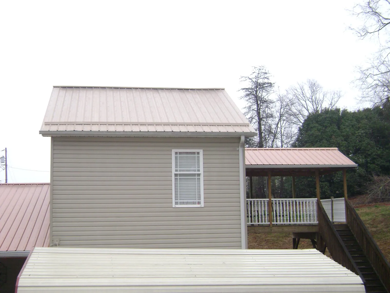 Tan metal roofs on a two story addition and attached porch, from a Roof Replacement job in Mc Donough
